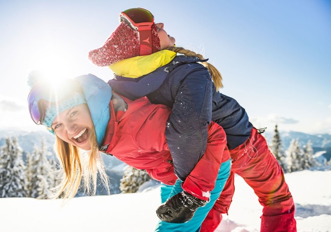 Zwei Menschen lachen und haben Spaß im Schnee an einem sonnigen Tag in den Bergen
