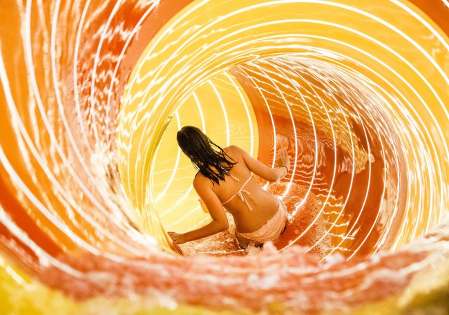 Eine Person rutscht in einem leuchtend gelben Wasserrutschentunnel