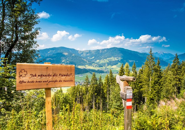Holzschild mit Spruch vor malerischer Berglandschaft und blauem Himmel