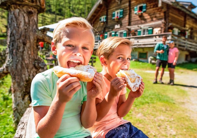 Zwei Kinder essen im Freien Bauernkrapfen vor der Prechtlhof