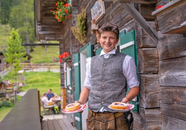 Ein Kellner im Trachtenoutfit serviert Dessert vor der Prechtlhütte