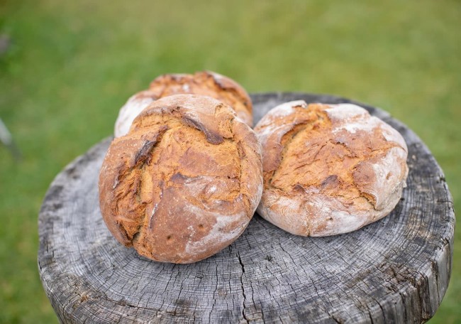 Drei runde Brote liegen auf einem alten Holztisch im Freien