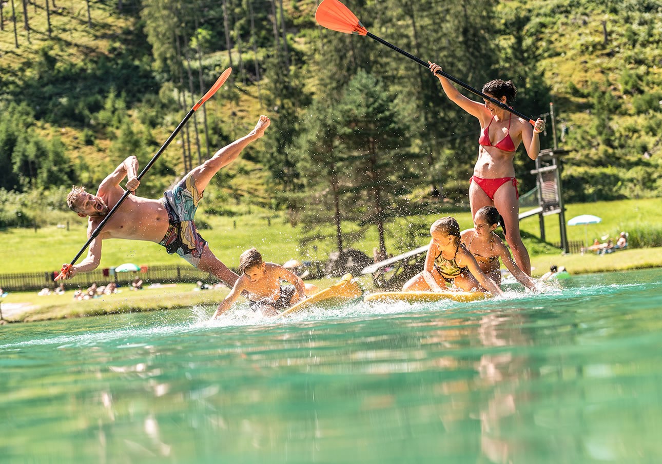 A man falls off a paddleboard as others play and paddle on a sunny day at the lake