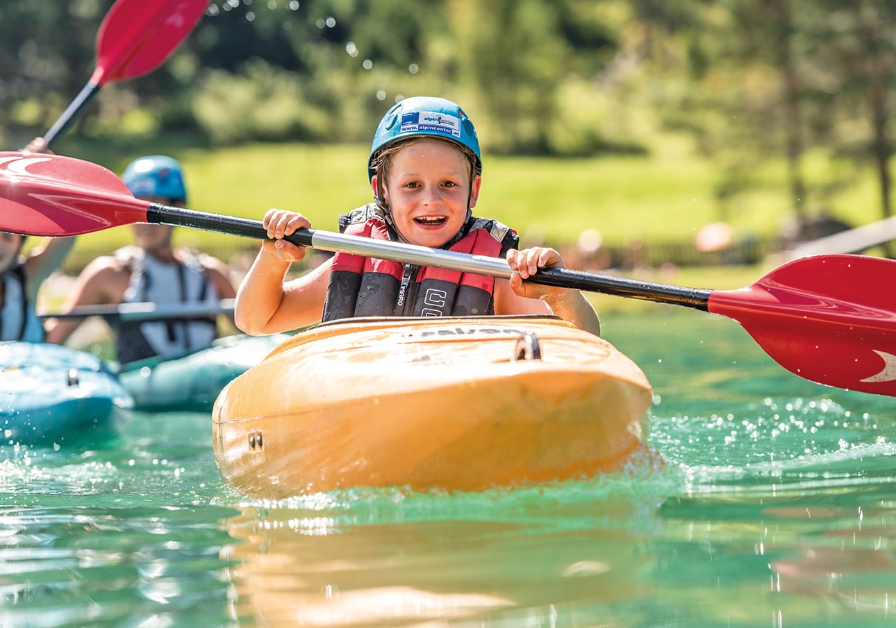 Young child kayaking on a sunny day, smiling while paddling on clear water