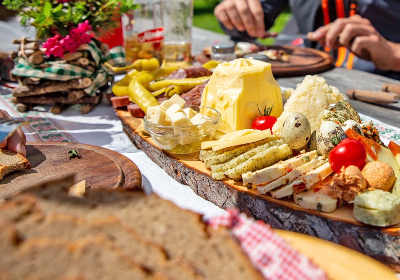 A rustic wooden platter filled with various cheeses, meats, vegetables, and bread