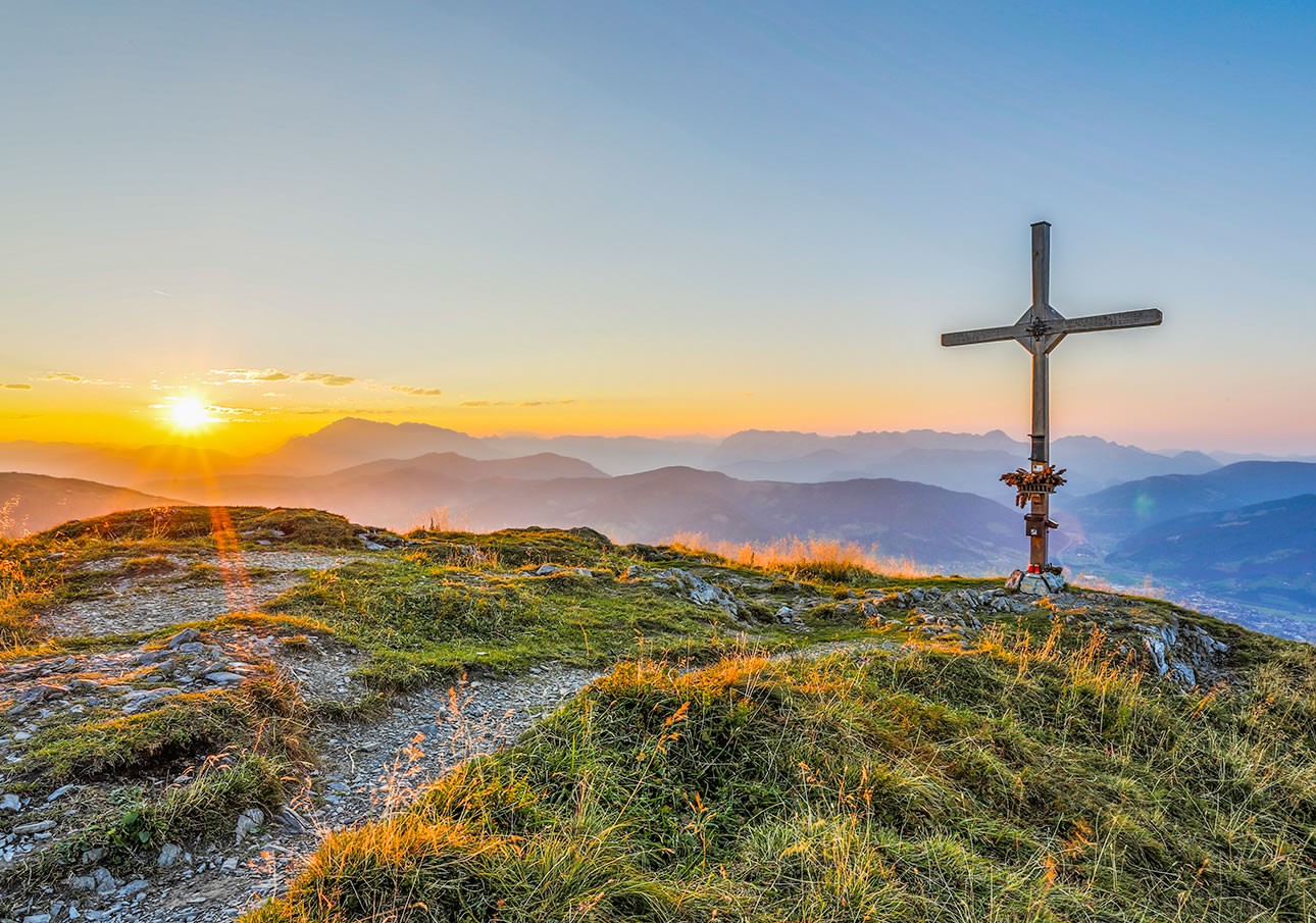 Sunset over mountains with a cross on a grassy hill