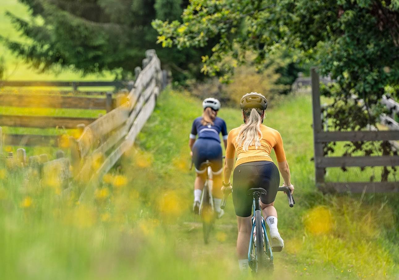 Zwei Radfahrerinnen fahren auf einem grasbewachsenen Weg durch die Natur.