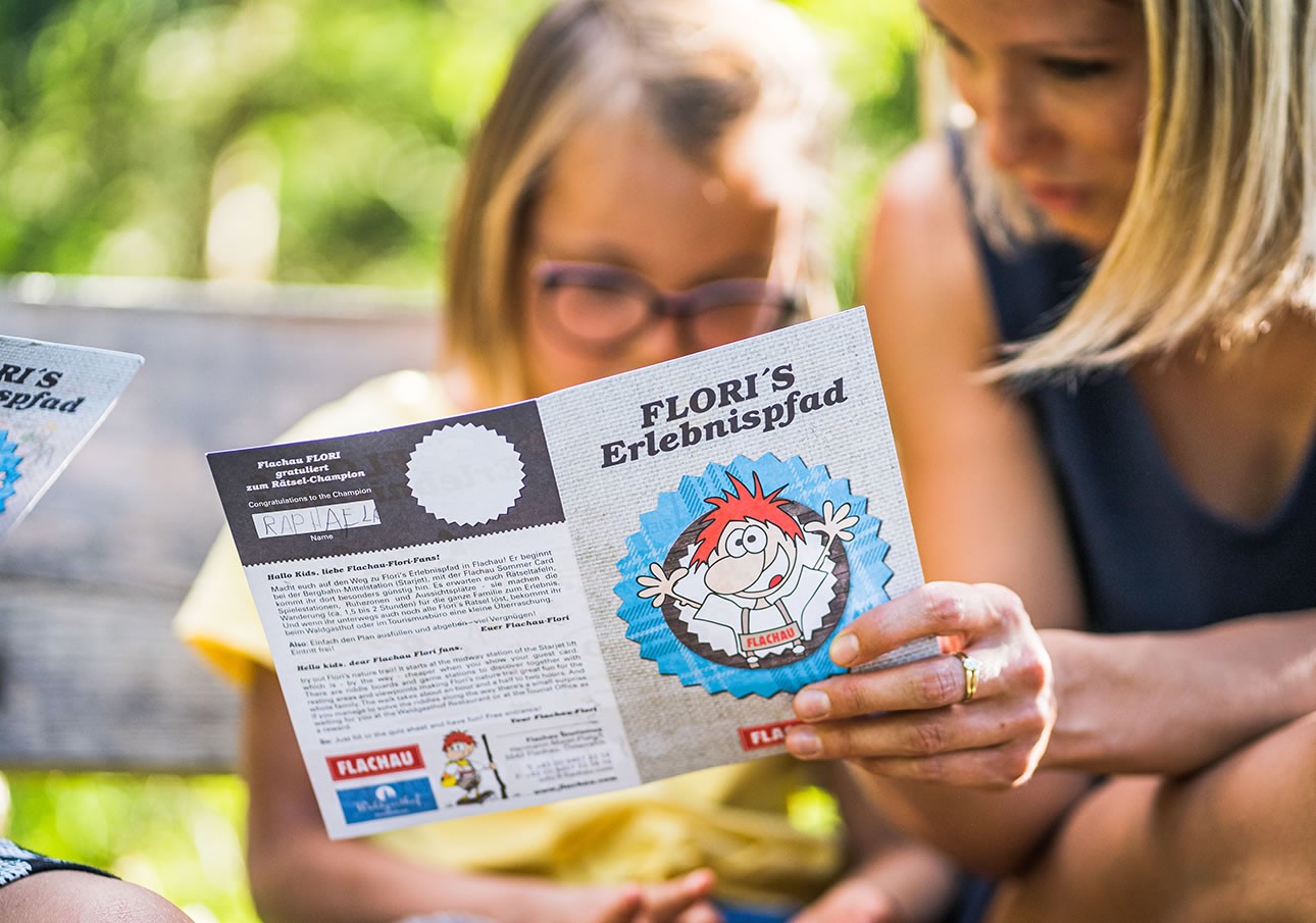 Eine Frau und ein Kind lesen gemeinsam einen Flyer mit der Aufschrift "FLORI'S Erlebnispfad"