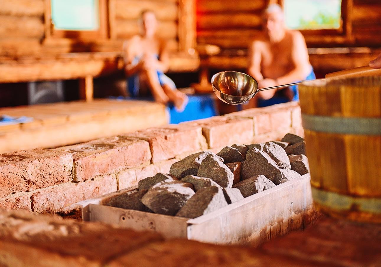 Heiße Saunasteine und ein Wasserschöpfer in einer Finnischen Sauna mit zwei Personen im Hintergrund